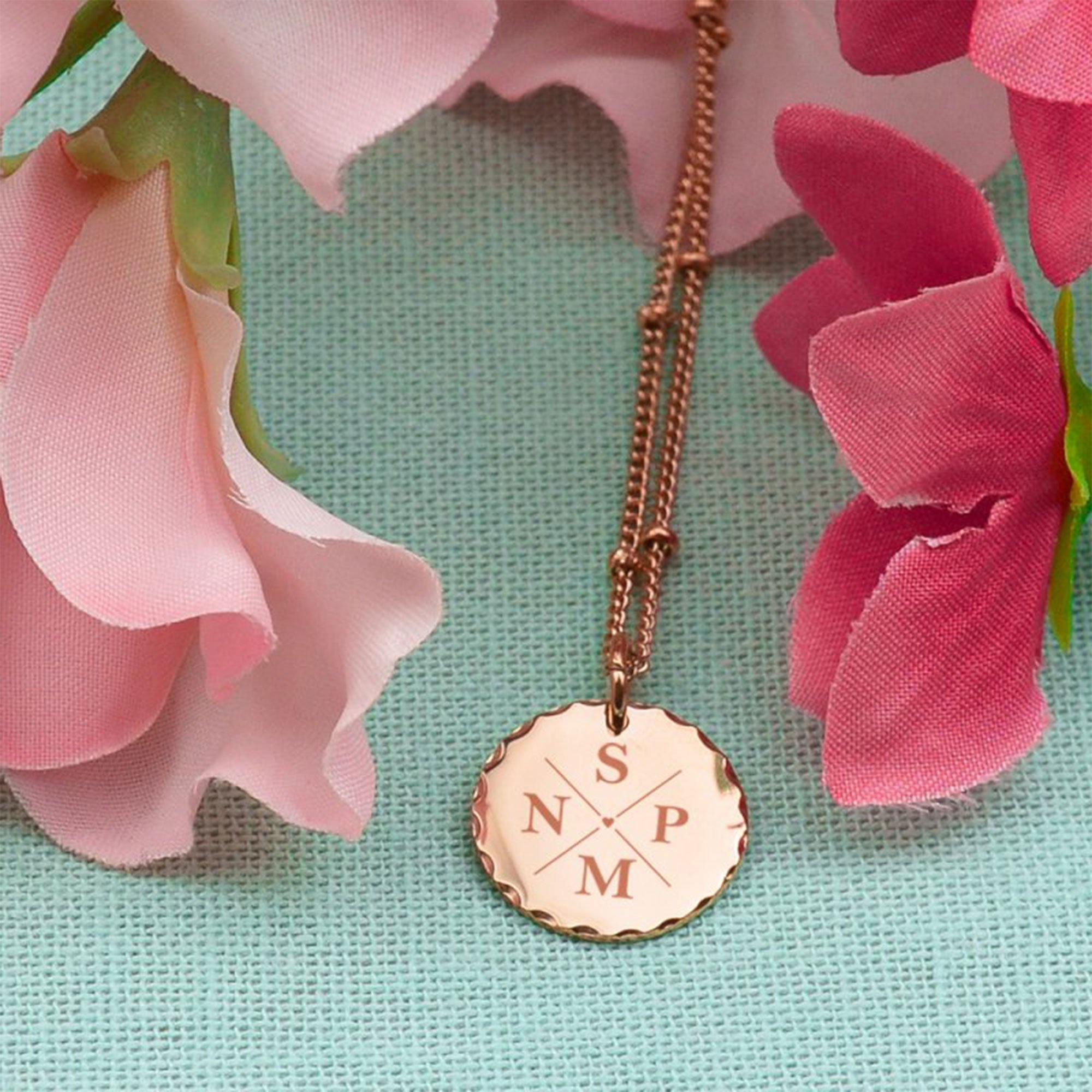 Necklace with name engraved in rose gold on a mint background with pink flowers