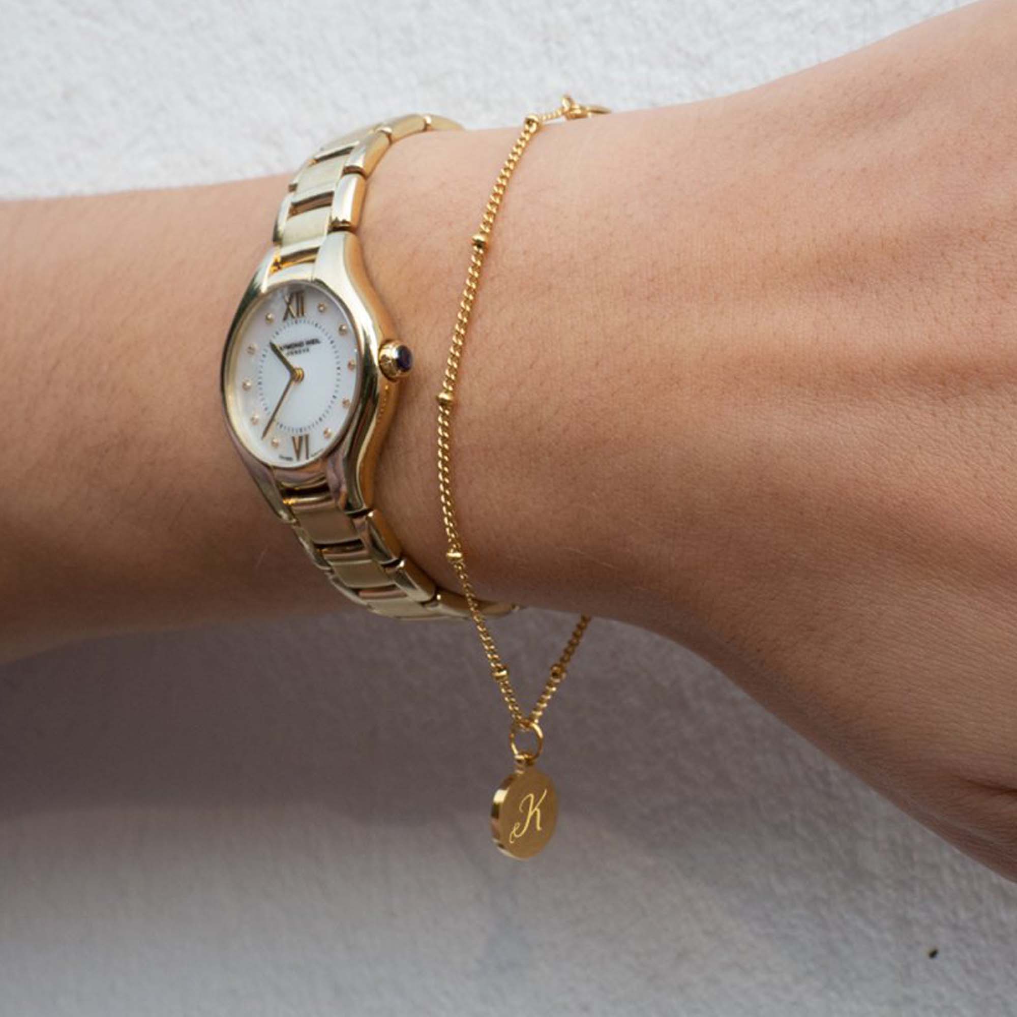 Armband mit einer Intiale in Gold am Handgelenk mit einer goldenen Uhr
