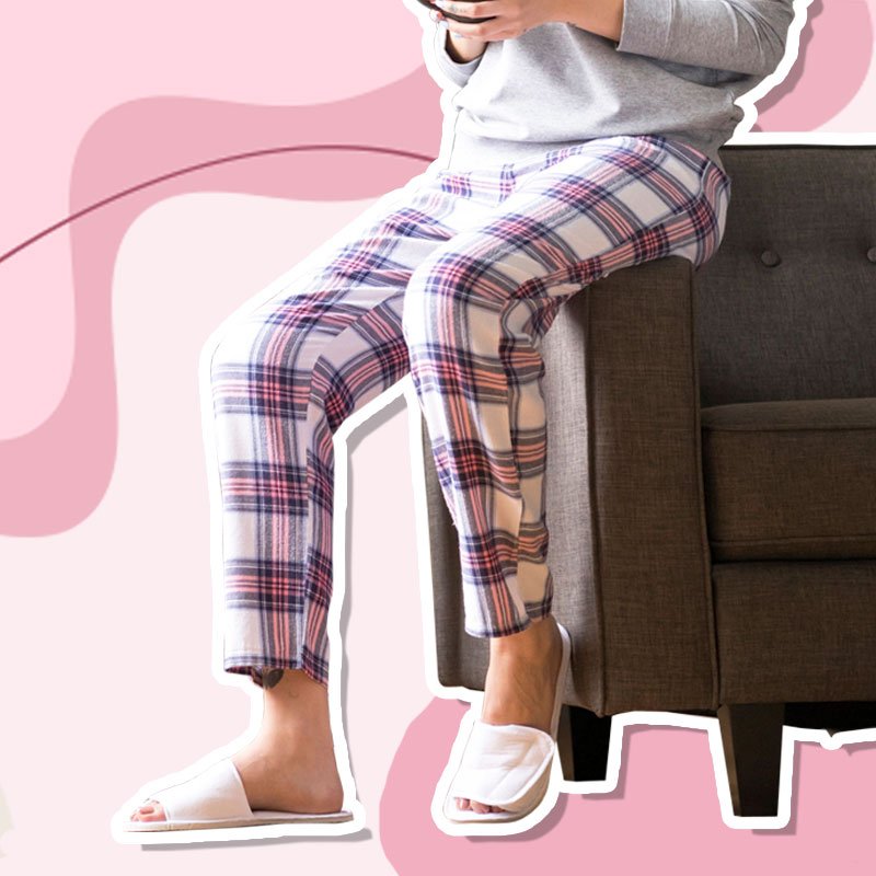 Vrouw met dames pyjama set op een sofa met een roze geruite pyjamabroek