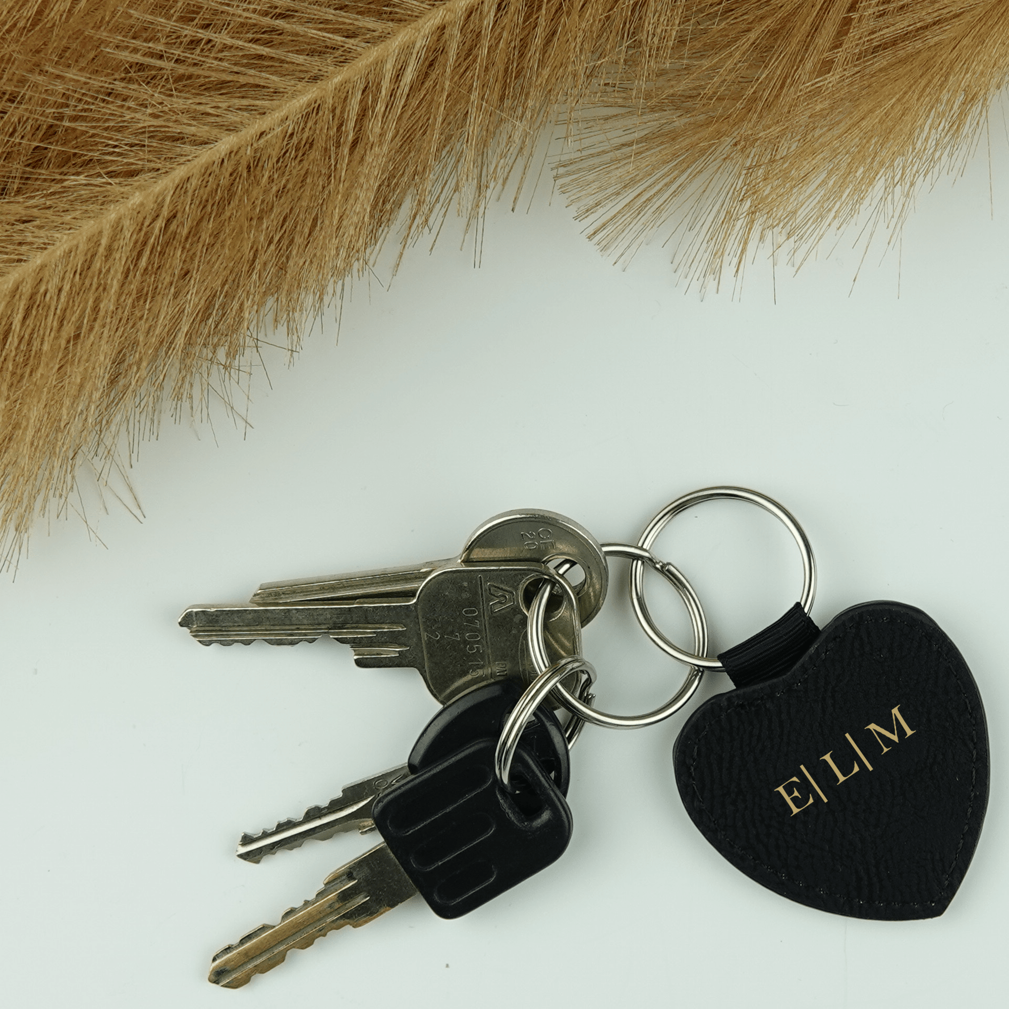 Black leather key fob engraved with initials on a white background with light brown branch